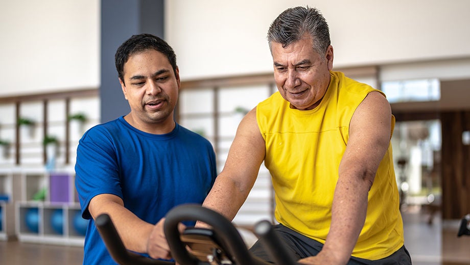 male sitting on a workout machine while a healthcare provider guiding him
